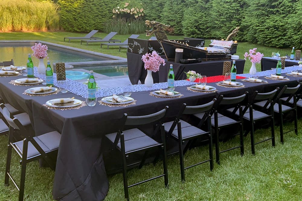 Outdoor hibachi party setup with table, chairs, and grill by a pool